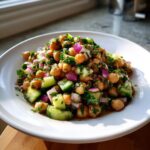 A vibrant bowl of dense bean salad featuring chickpeas, diced cucumber, red onion, and fresh herbs.